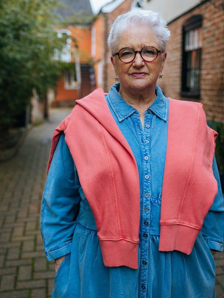 a woman in a blue shirt and a red jacket standing on a brick walkway